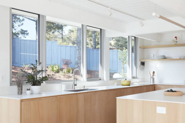 Natural color aluminum windows installed behind an ultra modern kitchen counter overlook a nicely kept yard