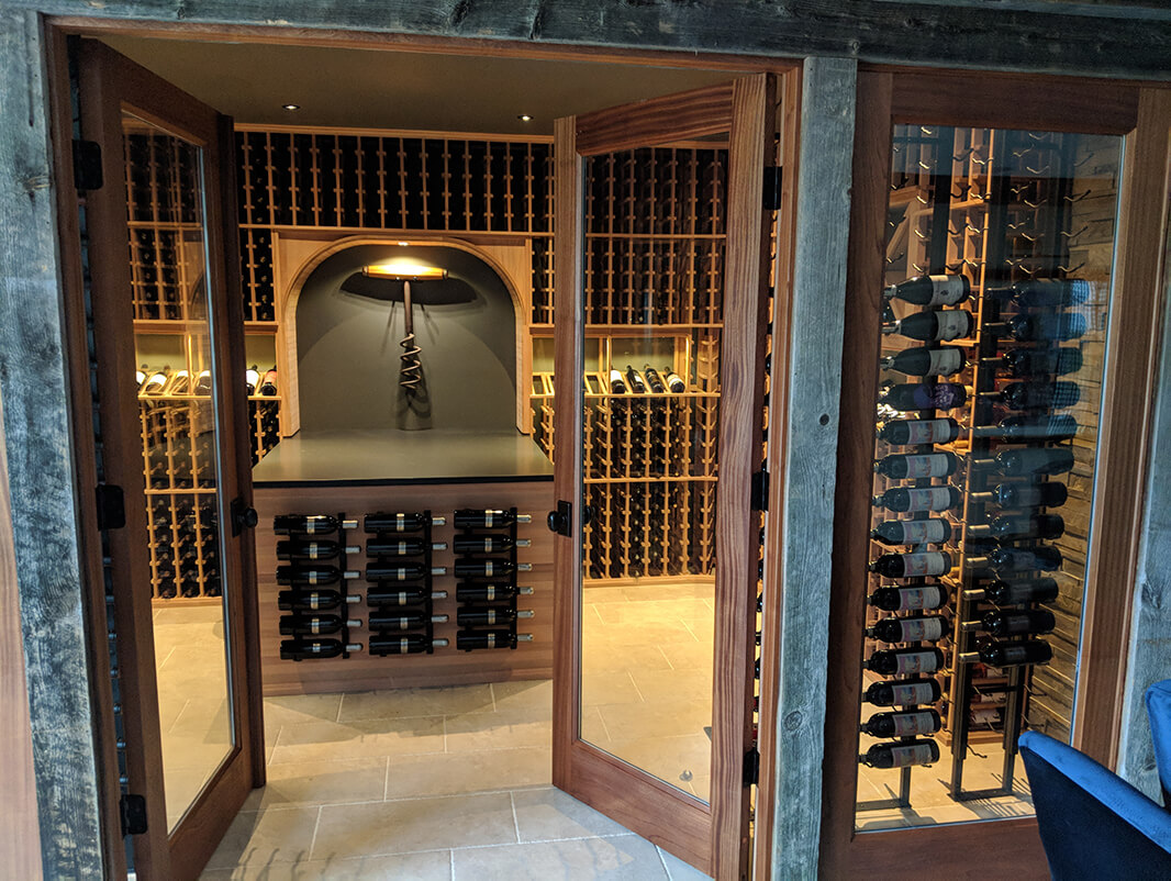 Custom wood doors containing large frames of clear glass installed in front of a fully stocked wine cellare