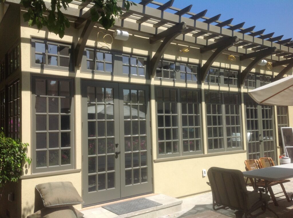 Exterior view of backyard with multiple wood windows installed and an attractive pergola jutting out from roof
