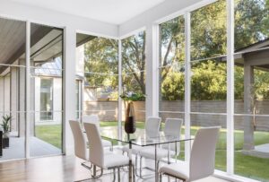 Floor to ceiling wood clad windows surround a white dining room table allowing for an unrestricted view of the back yard.