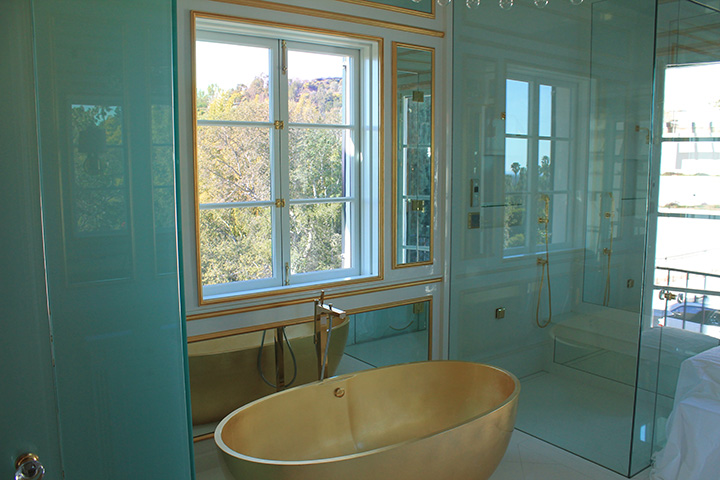 Beautiful bathroom with gold sunken tub surrounded by mirror and glass 