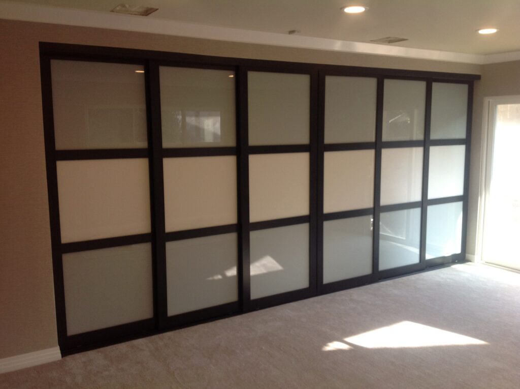 A large, multi-panel sliding wardrobe door with black frames and frosted glass.