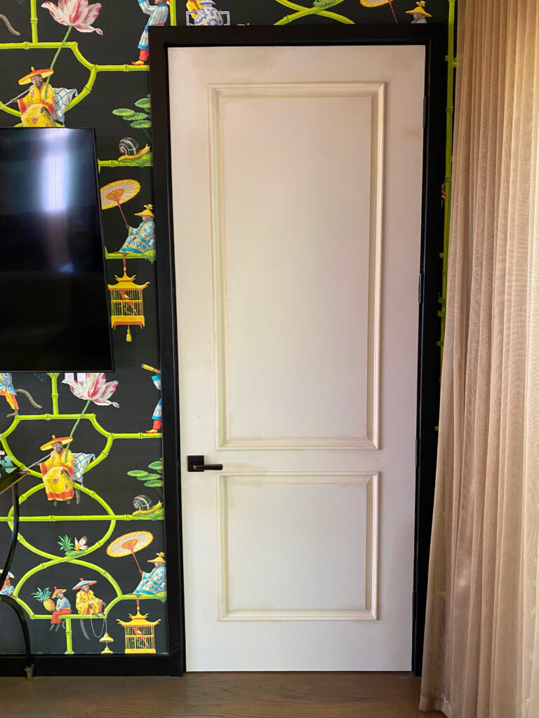 A traditional white panel door set against a wall with vibrant, colorful wallpaper.