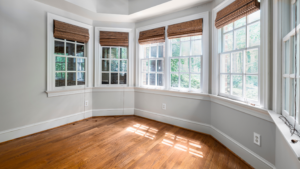 A bright, modern room with multiple large windows featuring white trim and wooden blinds, allowing natural light to stream onto the hardwood floors.