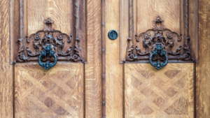 Intricately carved wooden double doors with vintage black knockers, showcasing the elegance of custom door craftsmanship.